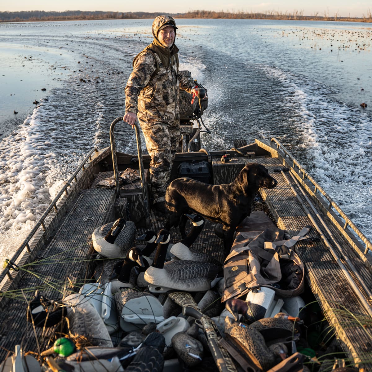 Hunter riding a boat with Hardcore Canada goose floater decoys on a cold river backwater