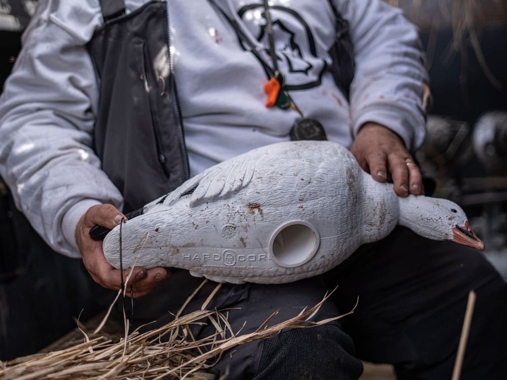 Hunter in white holding a Hardcore snow goose full body decoy with the Hardcore logo molded into its side